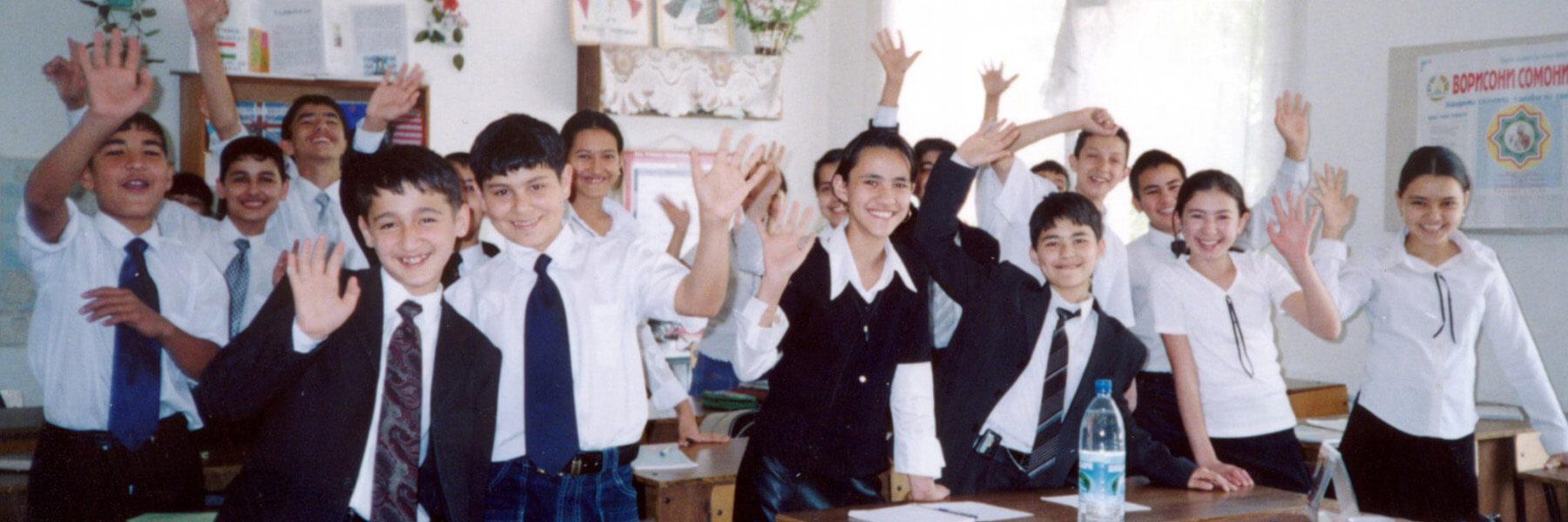 Students in a classroom waving to the camera.