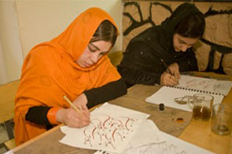 Two women write calligraphy on paper.