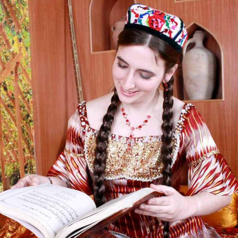 A girl in a Uyghr dress reading a book.