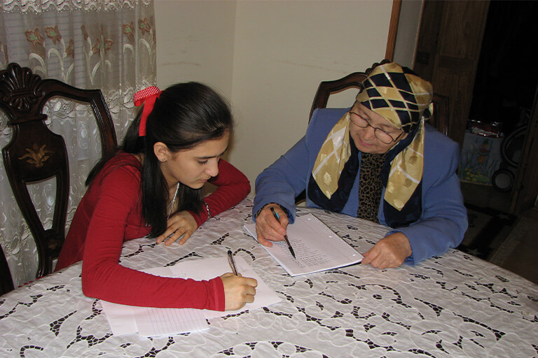 A young girl writing on paper with an older woman.