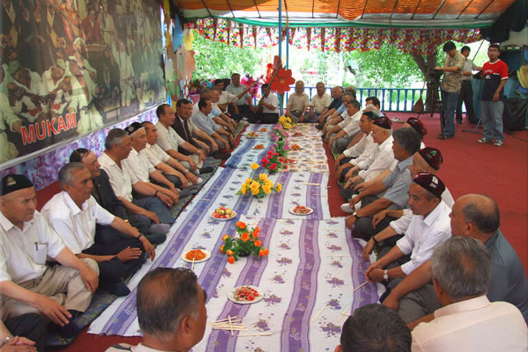 A group of people sitting along a large tablecloth.